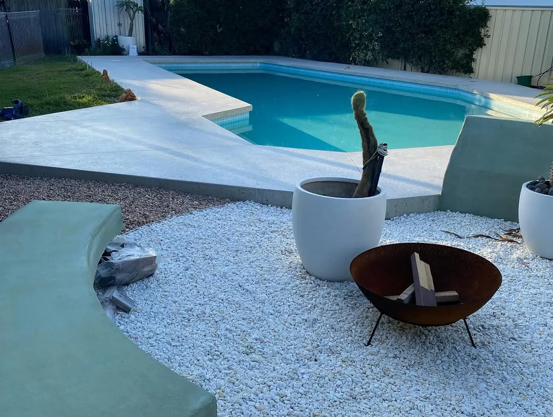 Round green concrete fire pit beside a polished pool surround
